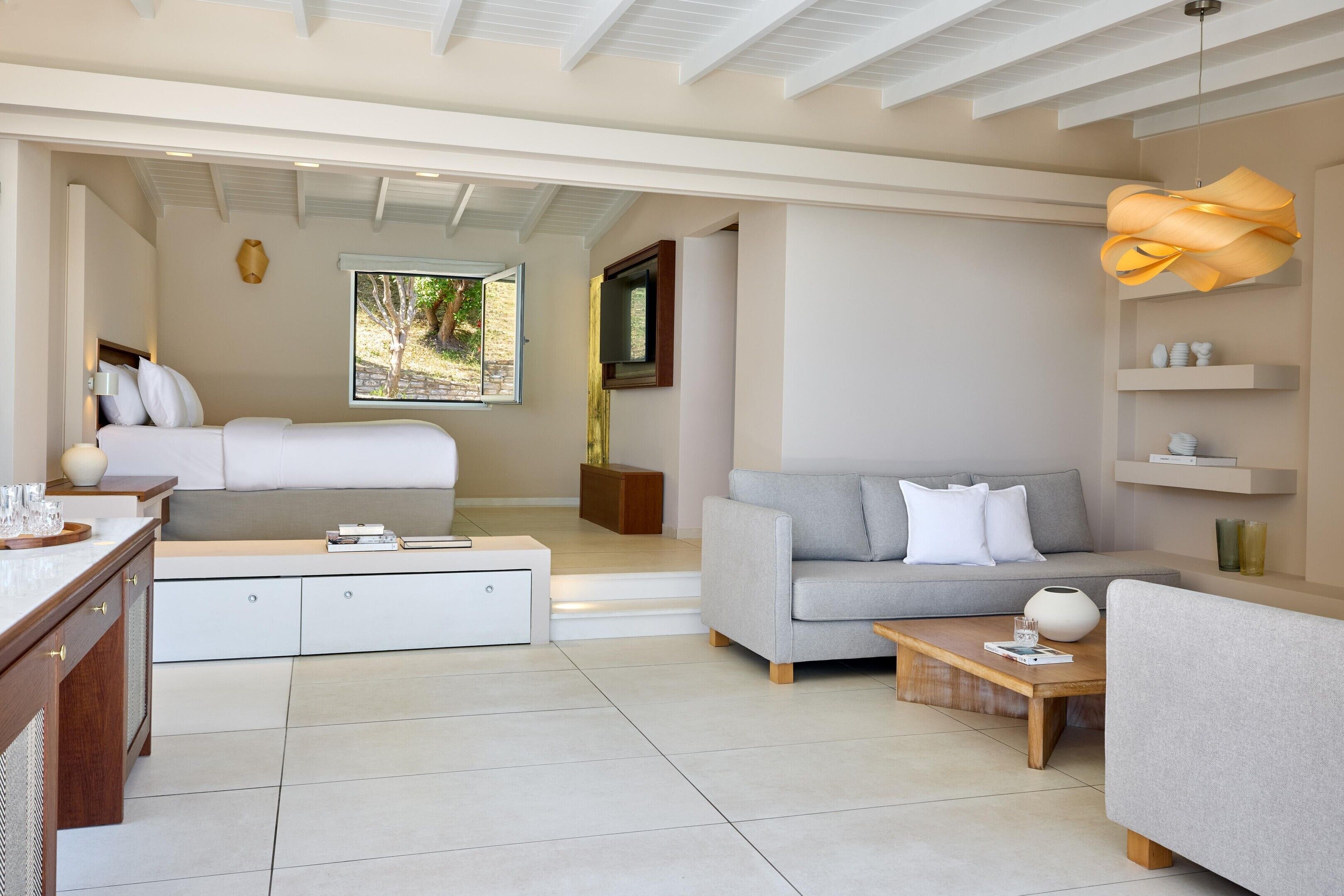 A modern, well-lit living room with a sofa, a coffee table, a TV, and a bed.