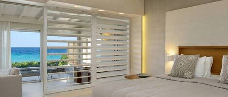 Une chambre moderne avec un grand lit, une vue sur l’océan et un balcon agrémenté de stores blancs.