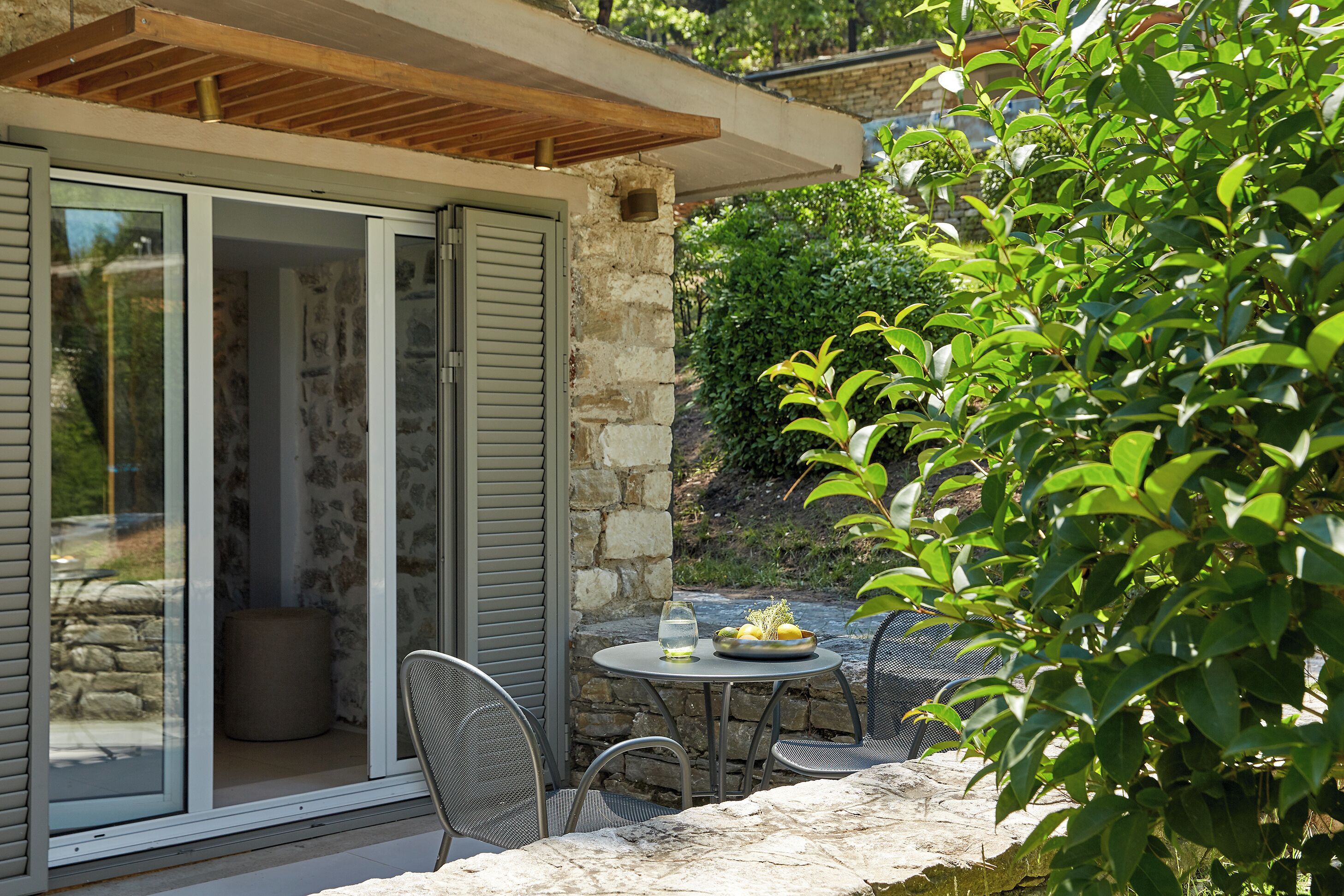 Une terrasse avec une table et des chaises, un mur en pierre et une porte-fenêtre coulissante donnant sur une pièce.