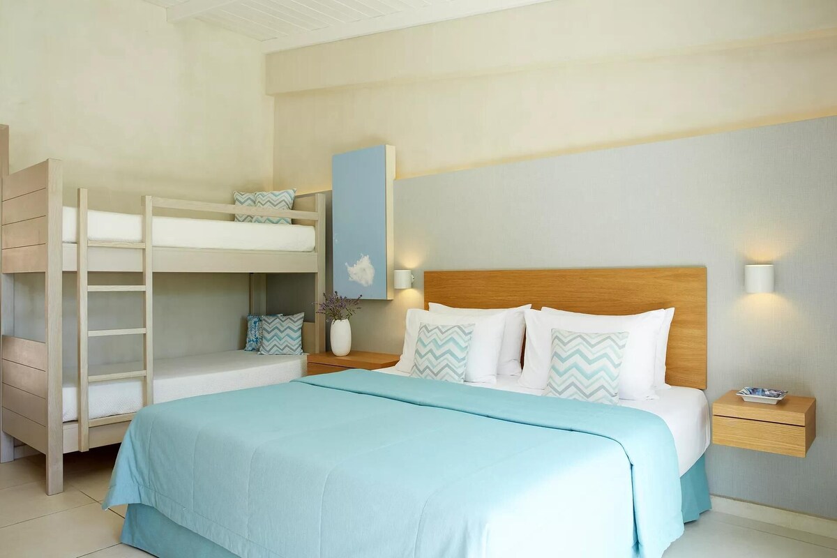 Un dormitorio con una cama litera, una cama individual, una mesita de noche, una lámpara y un estante fijado a la pared.