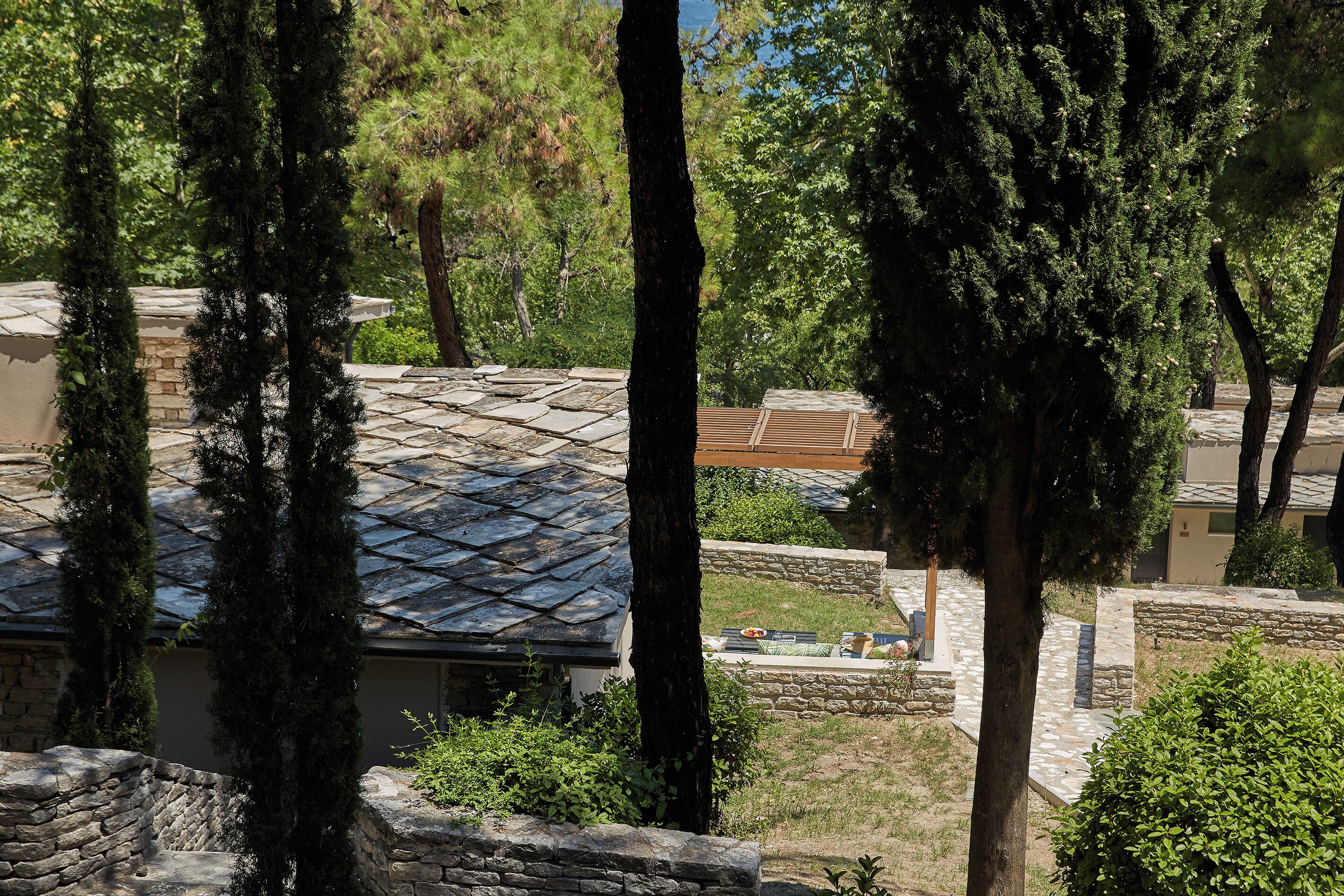 A residential area with stone walls, a paved patio, and a house with a sloped roof.