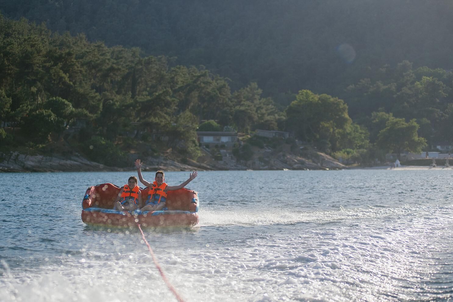 En vattensportaktivitet där man använder uppblåsbara flottar på en sjö, omgiven av träd och hus i bakgrunden.