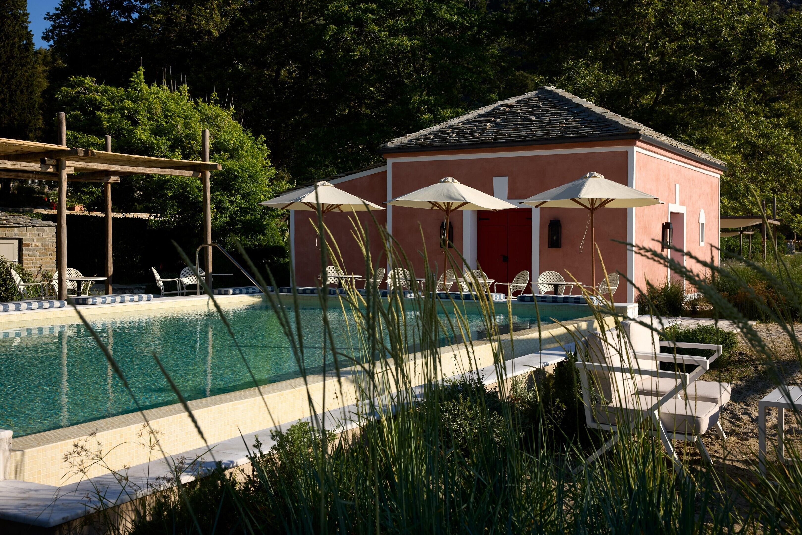 Un área de piscina con un edificio, asientos al aire libre y una pérgola.