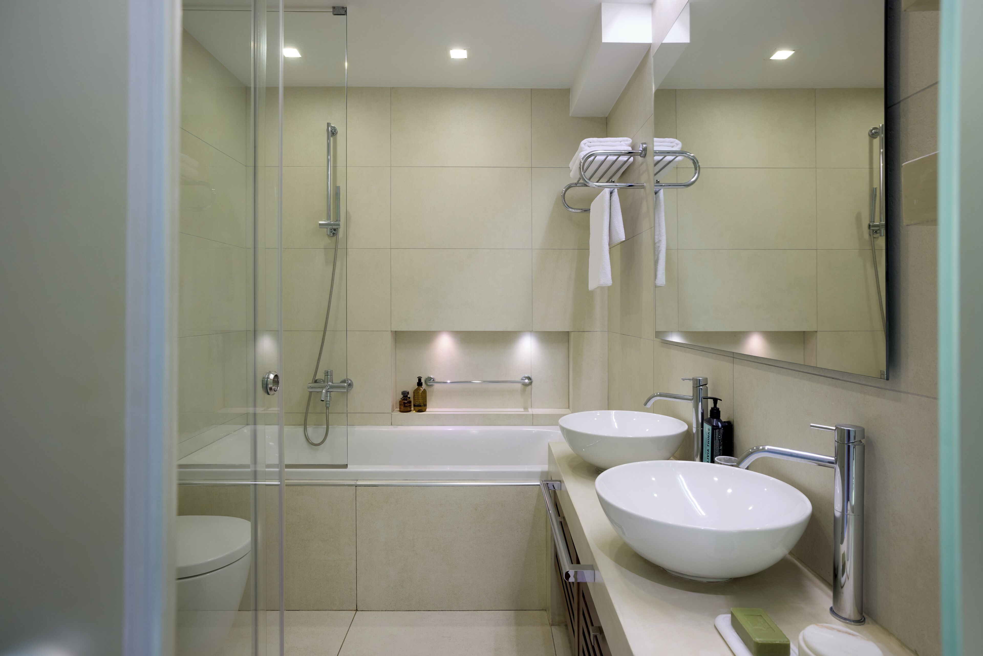 A modern bathroom with a glass-enclosed shower, a bathtub, two sinks, and a large mirror.