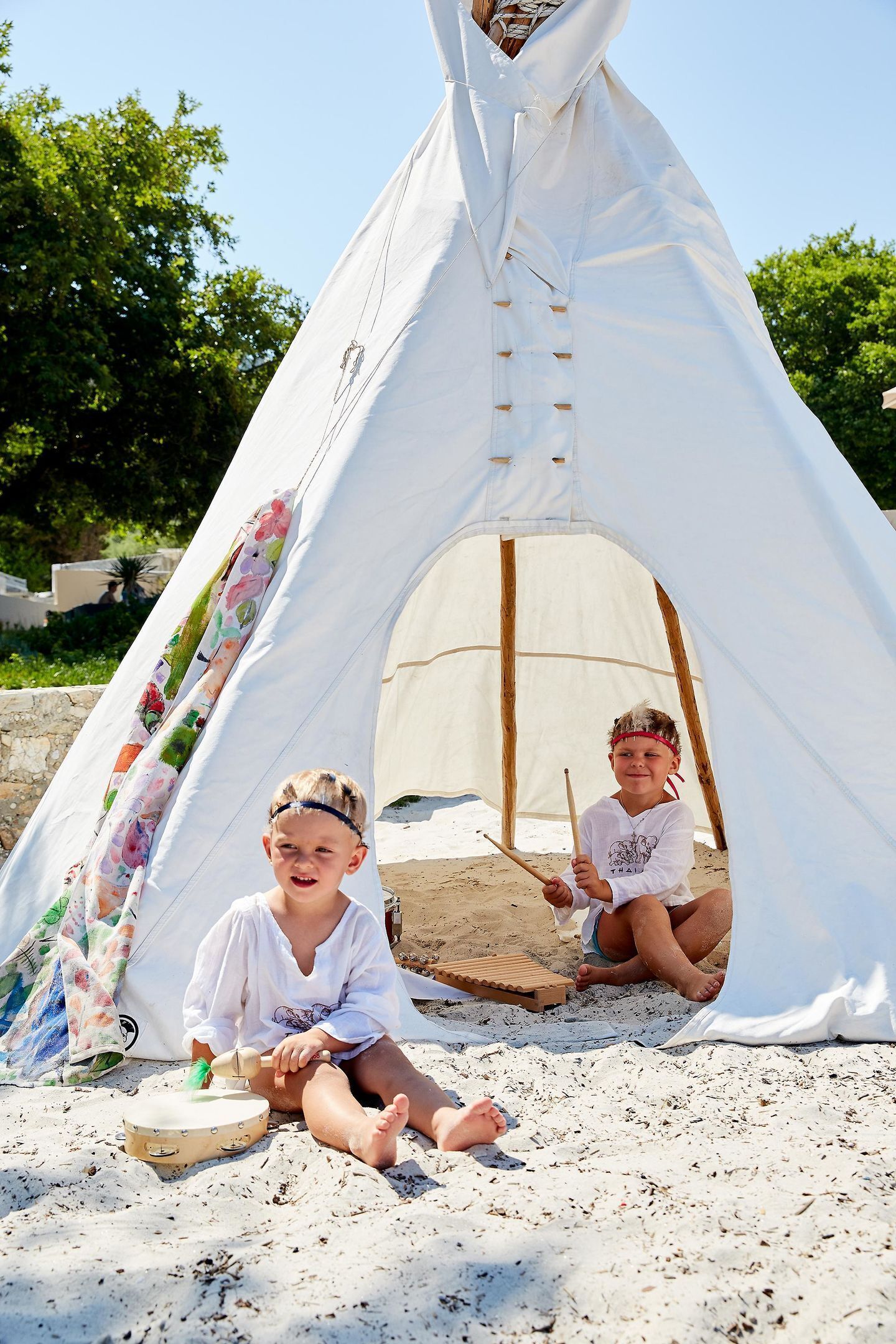 A white tent with a floral curtain on the side, set on a sandy beach with trees in the background.