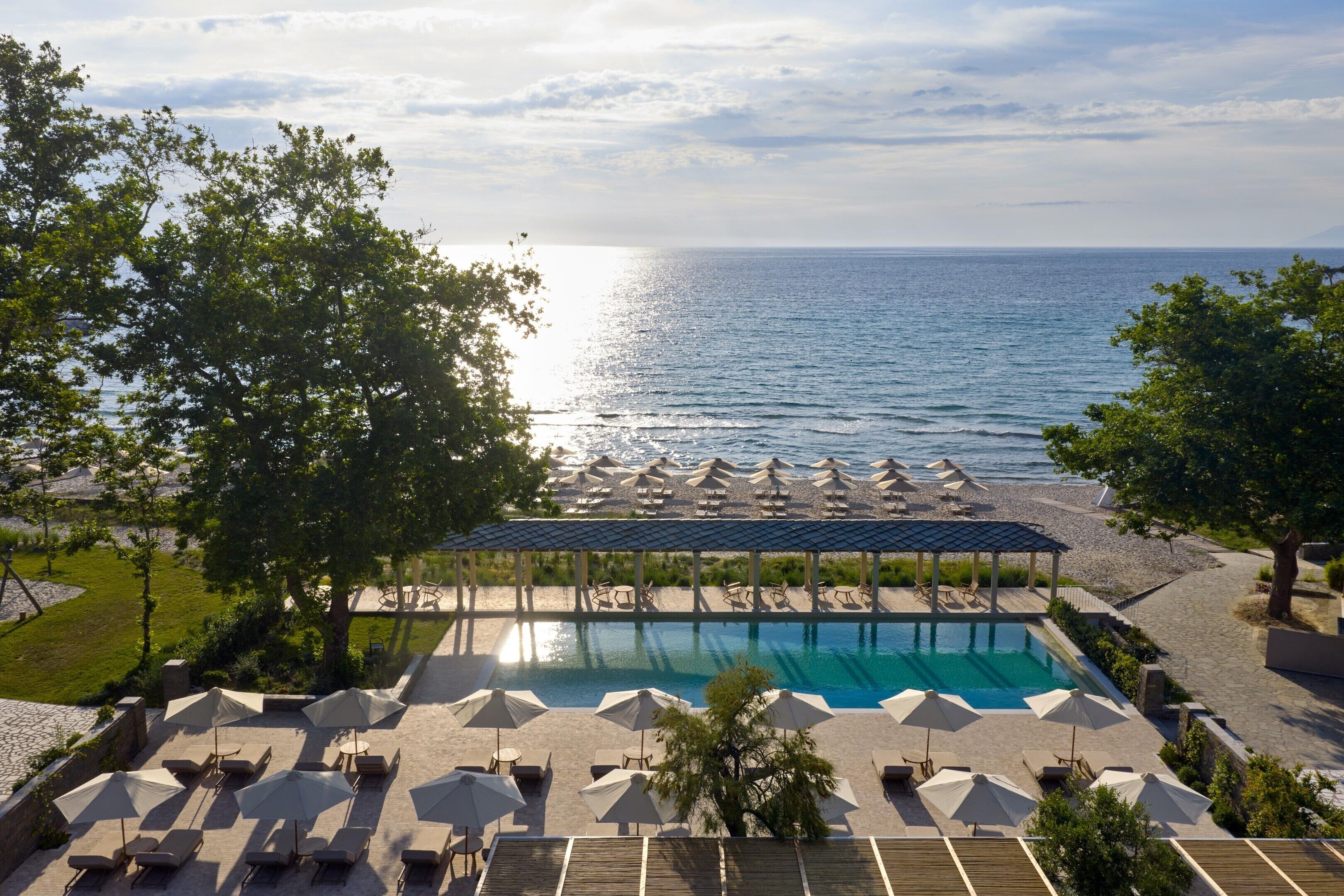 A pool area with lounge chairs and umbrellas, a covered seating area, and a view of the sea.