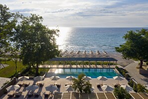 Zona de piscina con sillones de descanso y sombrillas, un área de estar cubierta y vista al mar.