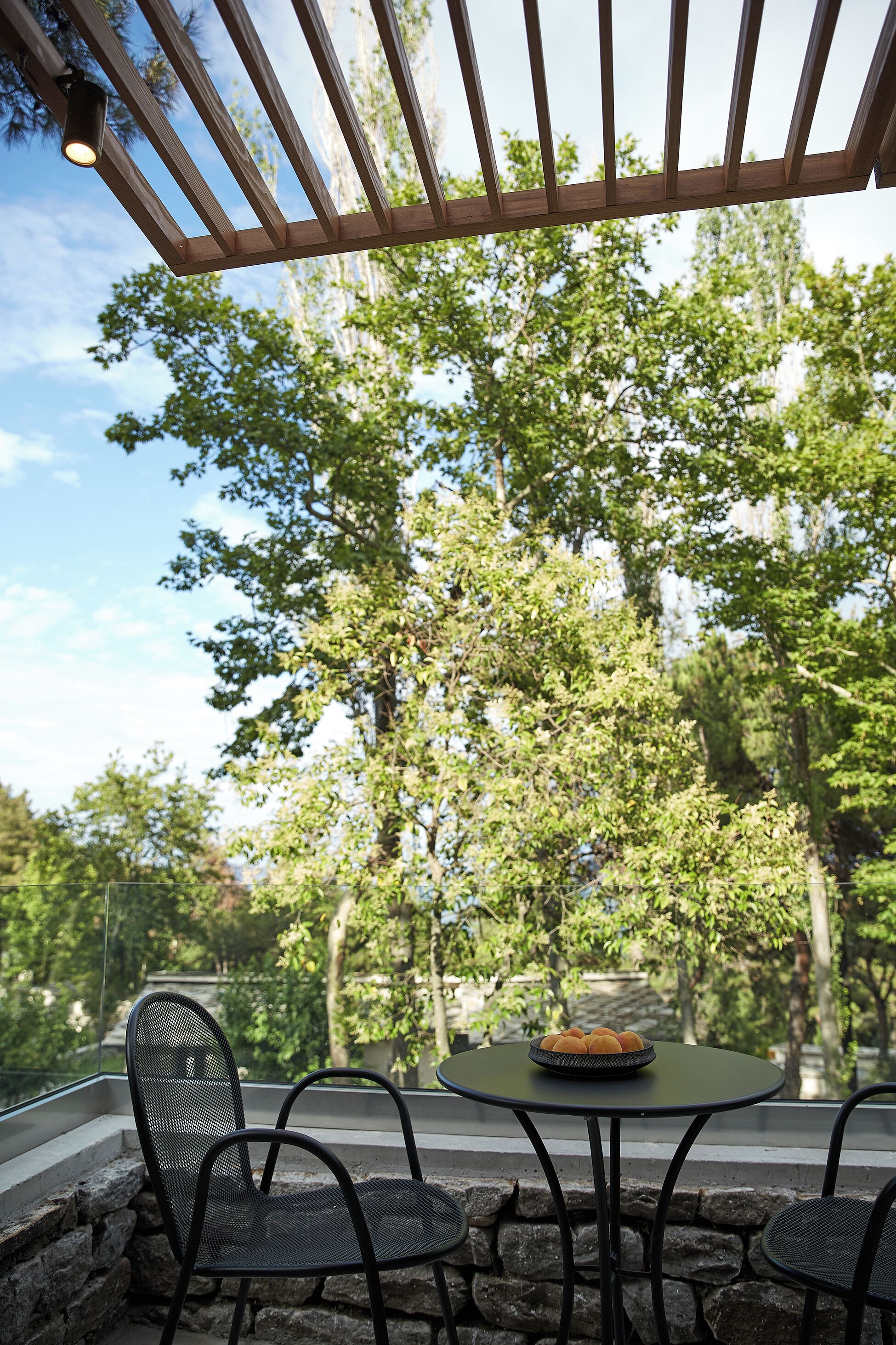 Eine Terrasse im Freien mit einem runden Tisch und Stühlen, umgeben von Steinmauern und Bäumen.