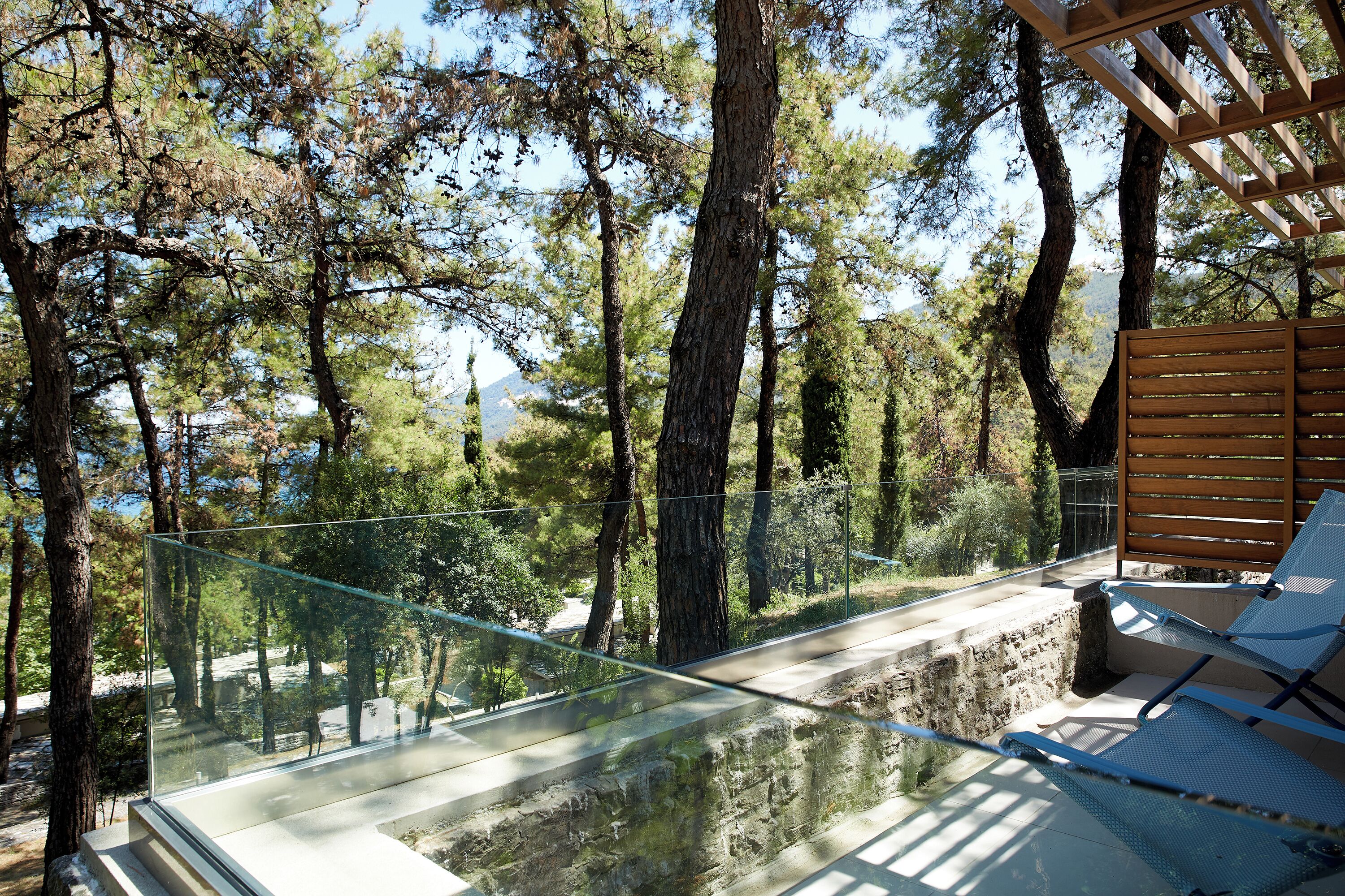 A glass bridge connecting two areas with a wooden deck and lounge chairs.