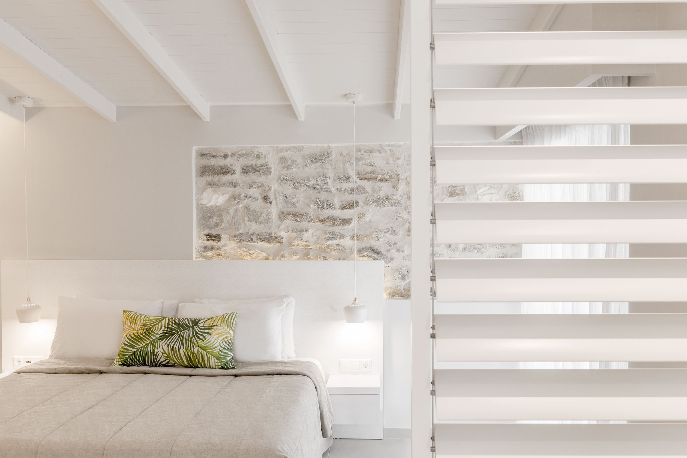 Une chambre à coucher avec un lit, une tête de lit blanche et un mur en pierre.