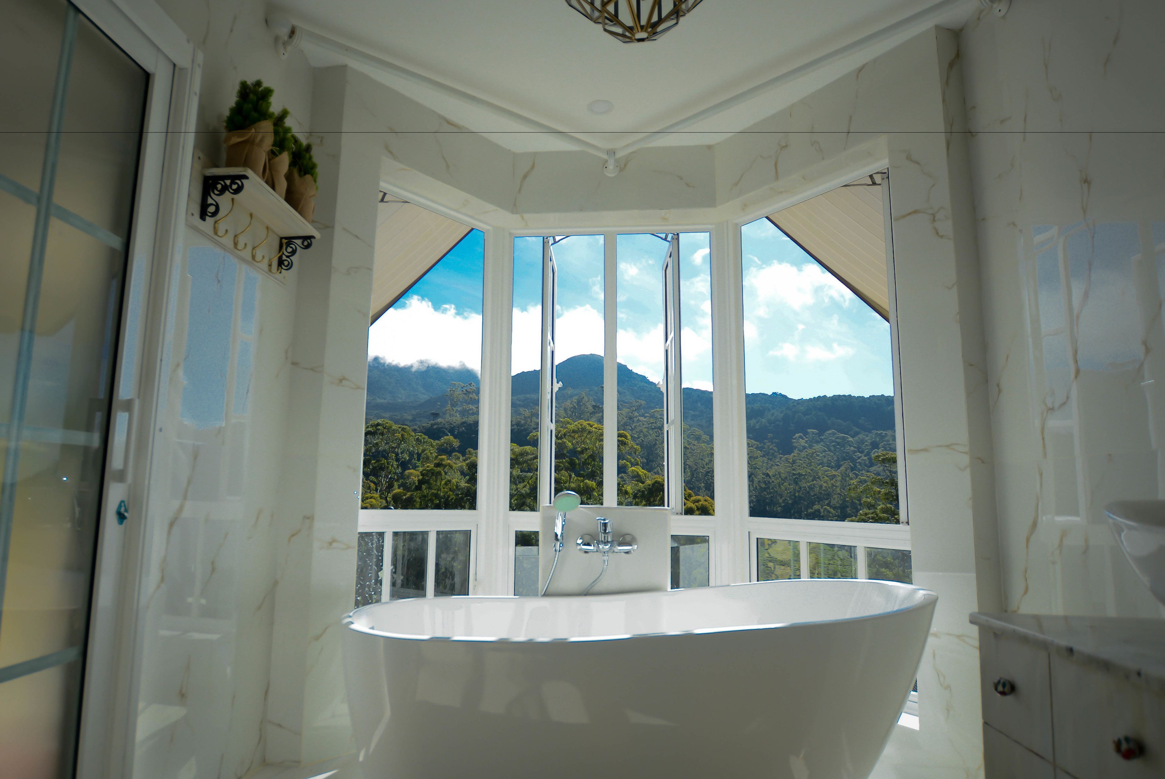A spacious bathroom with a large bathtub, a shower, and a view of a mountainous landscape through large windows.