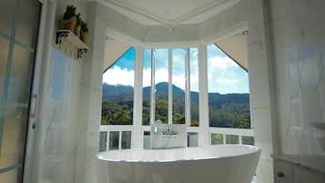 A spacious bathroom with a large bathtub, a shower, and a view of a mountainous landscape through large windows.