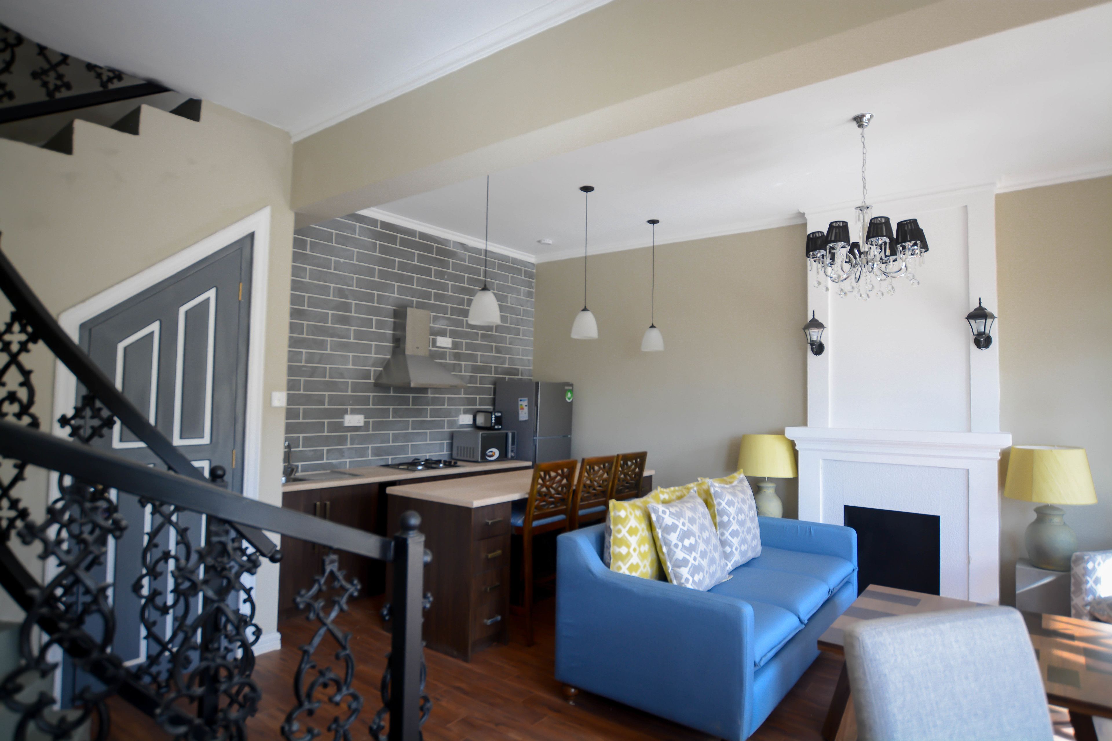 A living room with a blue sofa, a fireplace, and a kitchen area with a brick backsplash.