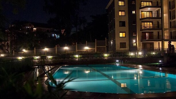 A nighttime view of a hotel with a swimming pool, multiple balconies, and a well-lit exterior. - Mayflower Serviced Apartments (Kampala)