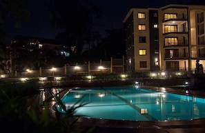 Vista nocturna de un hotel con piscina, varios balcones y fachada iluminada.