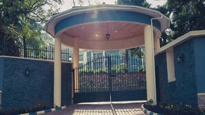 A covered entrance with a gated driveway, surrounded by stone walls and a paved path. - Mayflower Serviced Apartments (Kampala)