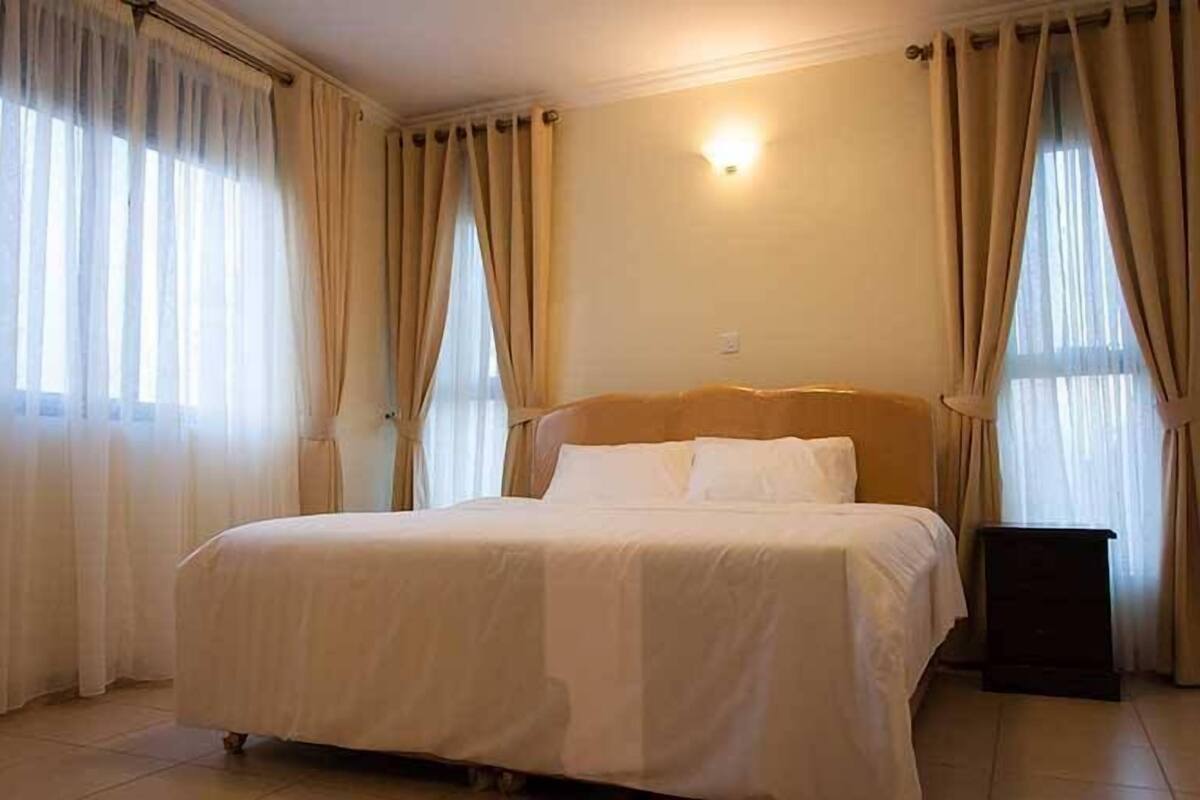 A hotel room with a large bed, beige curtains, and a wall-mounted light fixture.