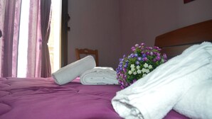 A bed with a purple bedspread, a rolled white towel, and a bouquet of purple and white flowers. - B&B Mannala' (Agrigento)