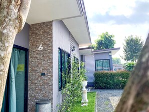 A modern building with a stone facade, a number '6' sign, and a small garden area with a decorative urn and a tree. - Lamer Ville Resort (Chanthaburi)