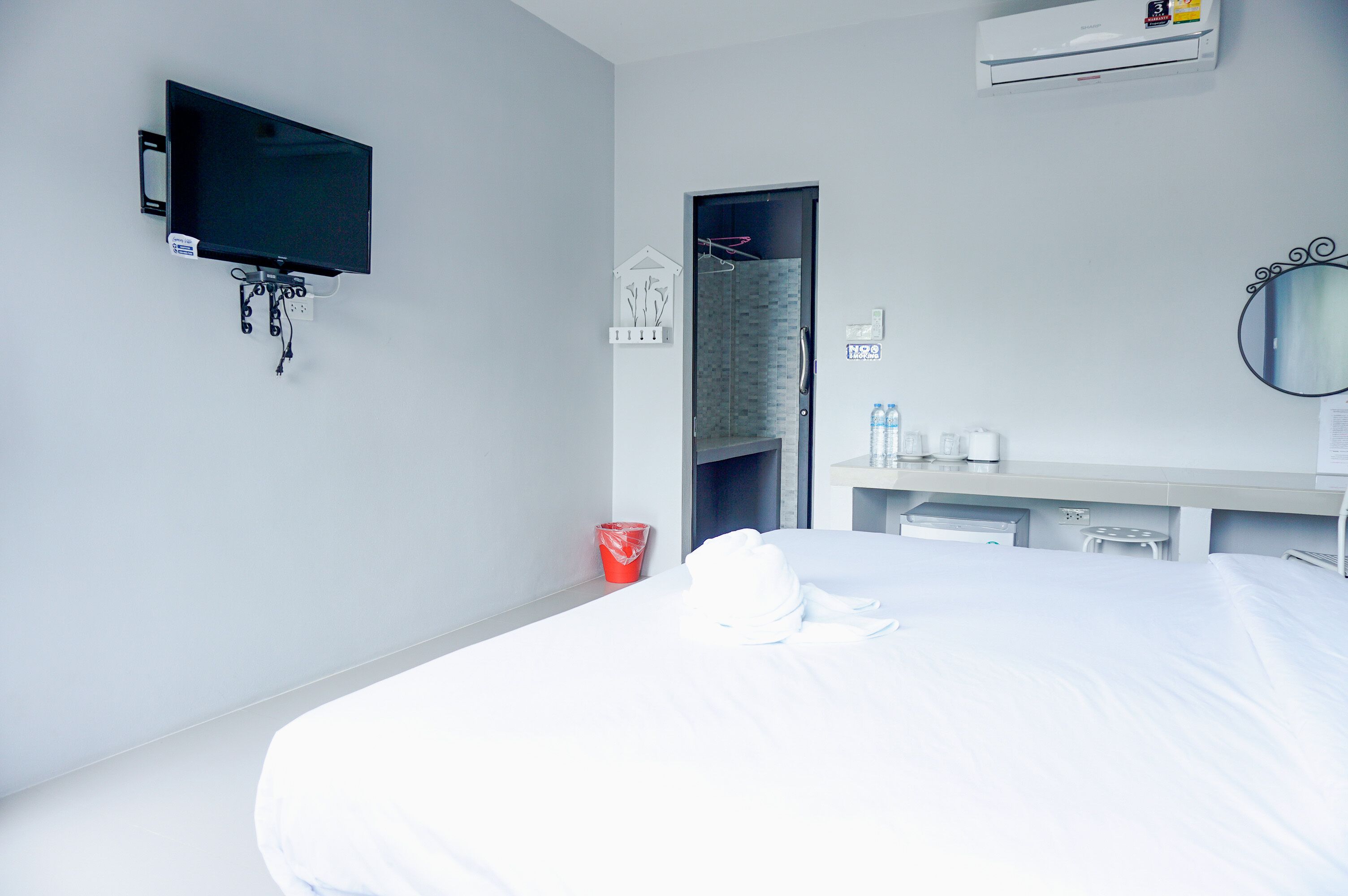 Habitación de hotel con una cama, televisión montada en la pared, zona de ducha, tocador con espejo y un cubo de basura rojo.