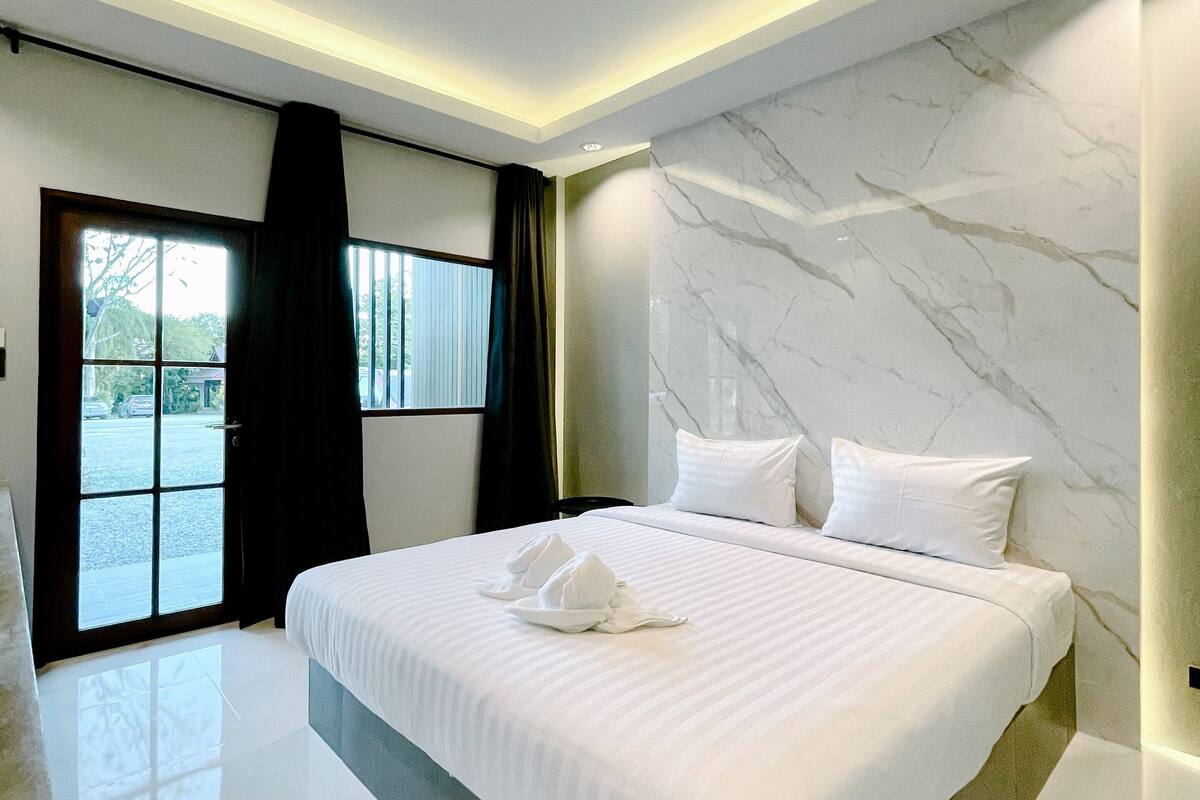 A modern hotel room with a large bed, marble wall, and a view through the window.