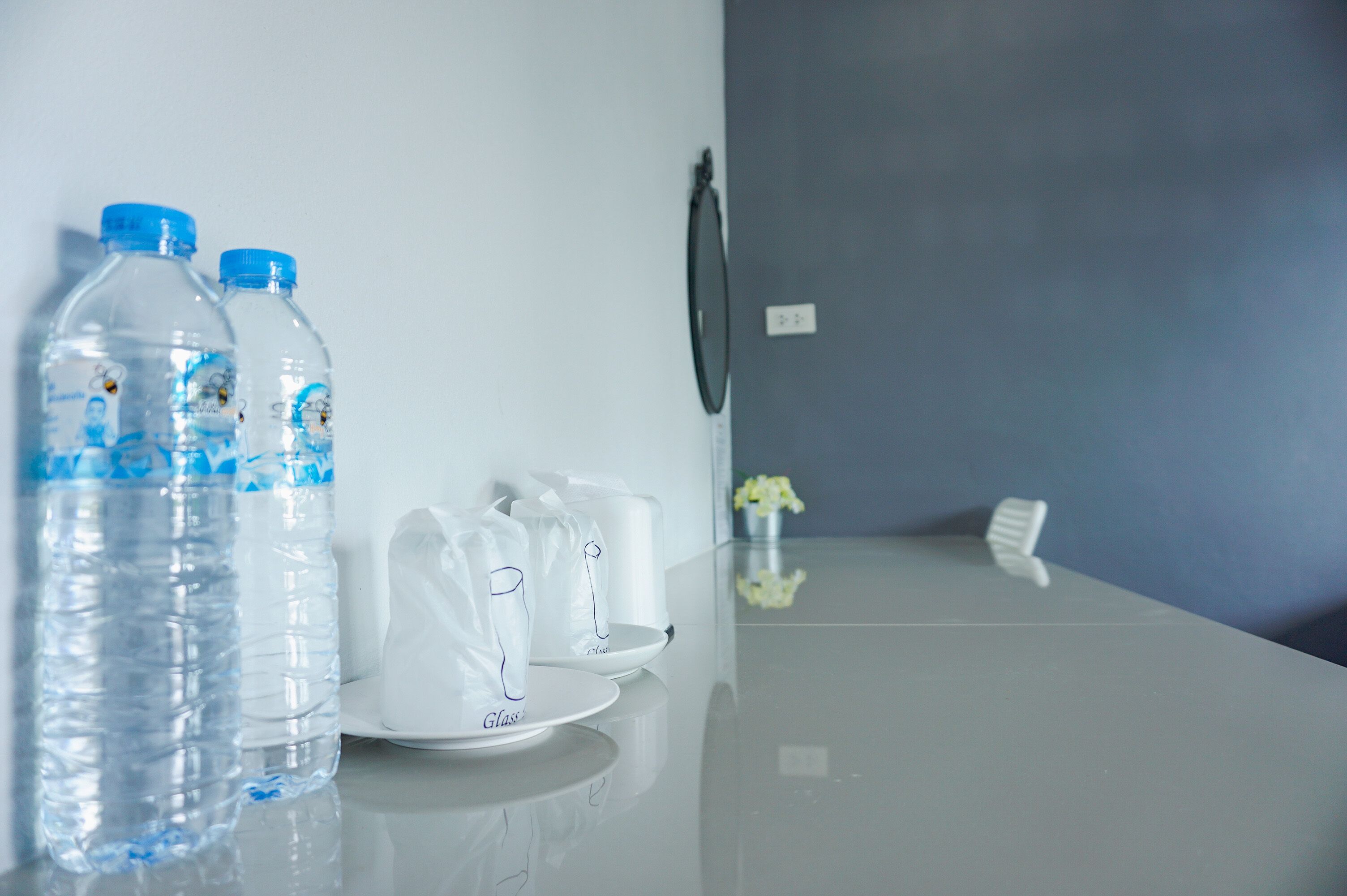 A clean, modern hotel room with a white table displaying water bottles, a glass, and a white bag.