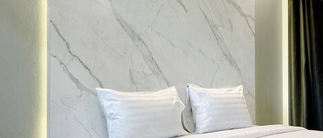 Un dormitorio moderno con una cama grande, ropa de cama blanca, una pared con diseño de mármol y una pequeña mesa redonda.