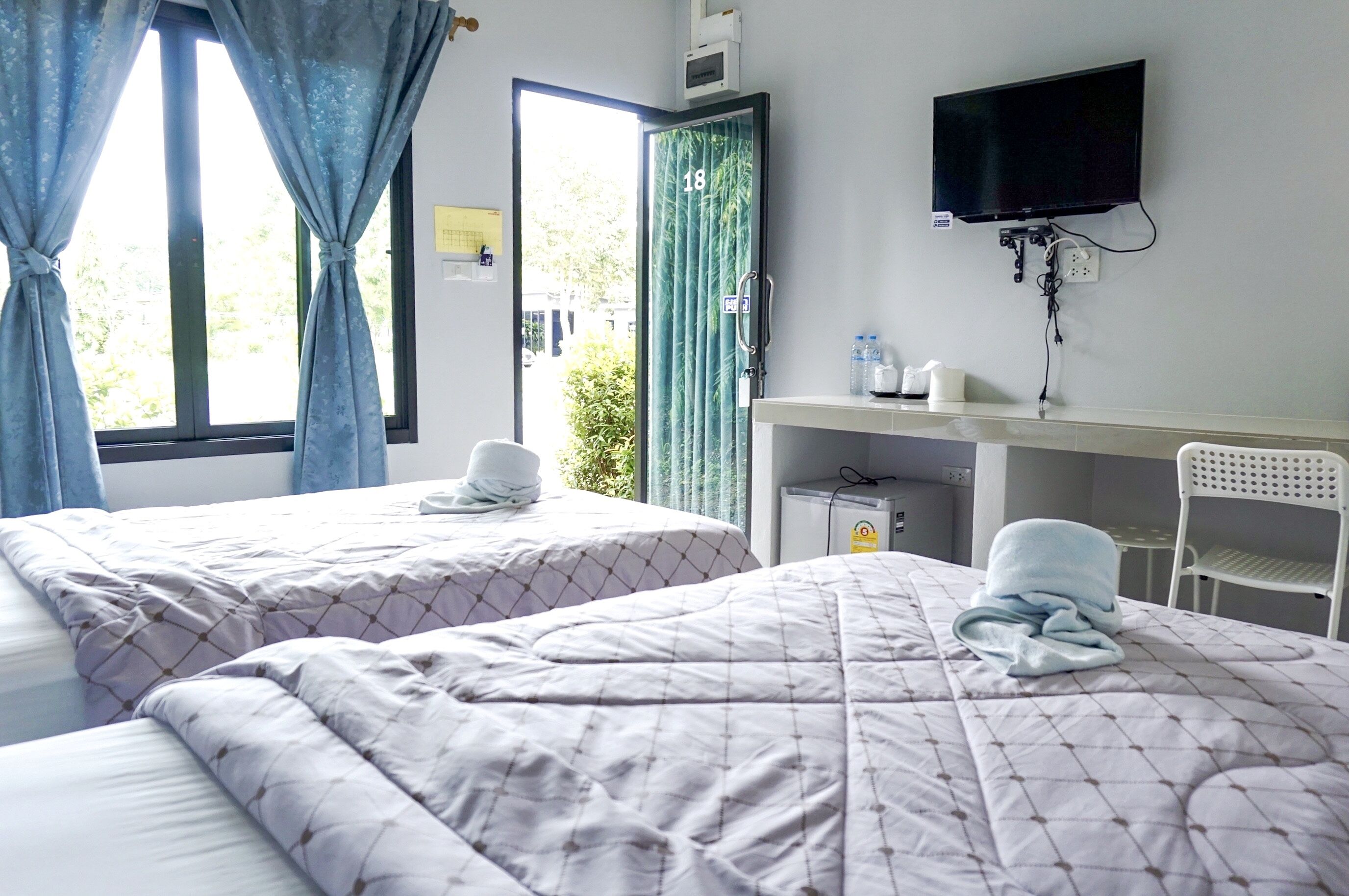 A hotel room with two beds, a TV mounted on the wall, a desk with a chair, and a window with curtains.