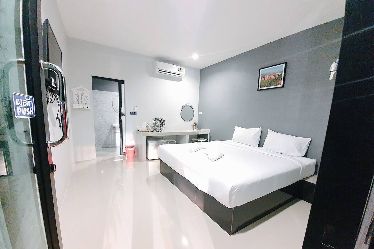 A modern hotel room with a large bed, a desk, and a small bathroom.