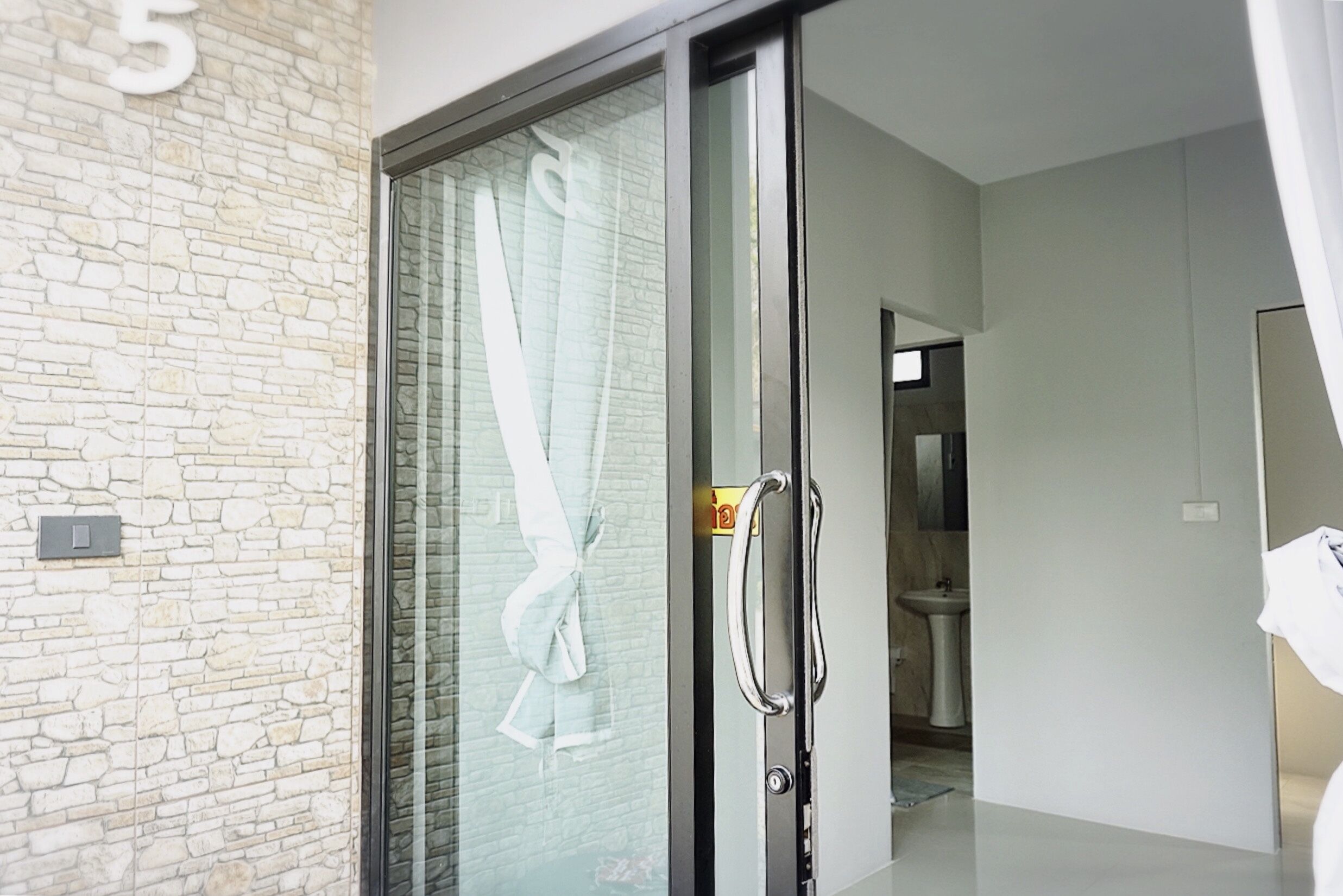 A modern interior with a stone wall, a glass door with a towel hanging, and a visible bathroom with a sink and mirror.