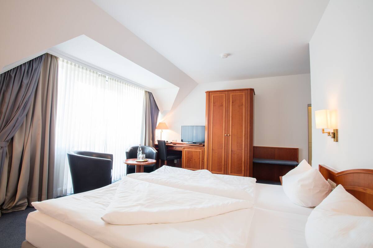 A hotel room with a large bed, a desk with a chair, a television, and a wardrobe.