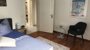 A bedroom with a bed, a chair, a small table, and a door leading to another room. - Villa Kaissini (Orselina)