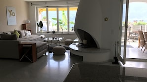 A modern living room with a built-in fireplace, large windows with yellow curtains, a sofa, and a coffee table. - Villa Kaissini (Orselina)