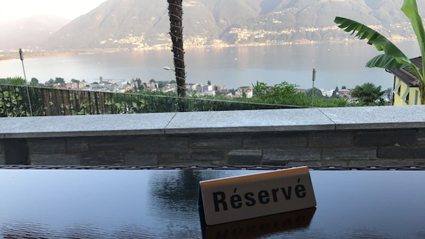 A sign reading "Réserve" in front of a body of water with a cityscape and mountains in the background. - Villa Kaissini (Orselina)