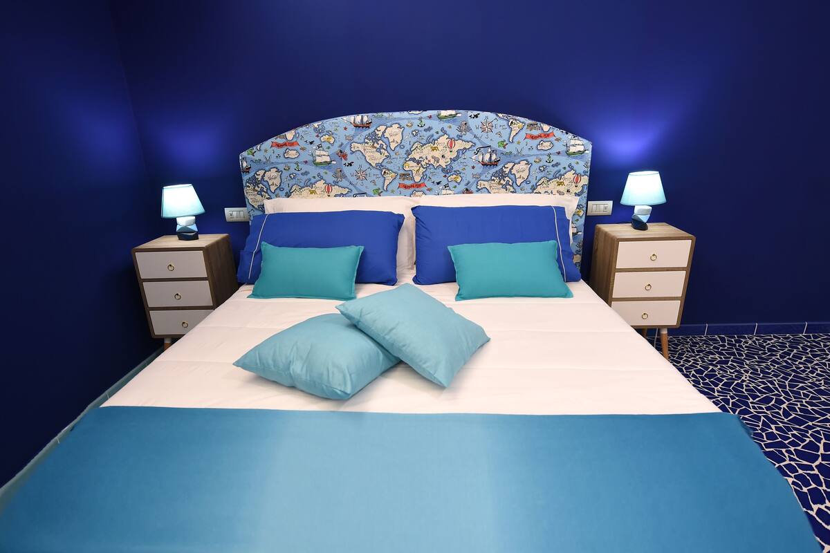 Un lit avec une tête de lit à motifs, deux tables de chevet avec des lampes et une couvre-lit bleue et blanche.