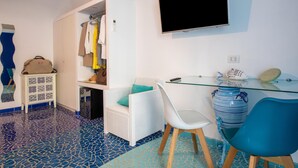 A room with a tiled floor, a white wicker chair, a glass table, a TV mounted on the wall, and a wardrobe with hanging clothes. - Aquae Romanae Bed and Breakfast Sorrento (Sorrento)