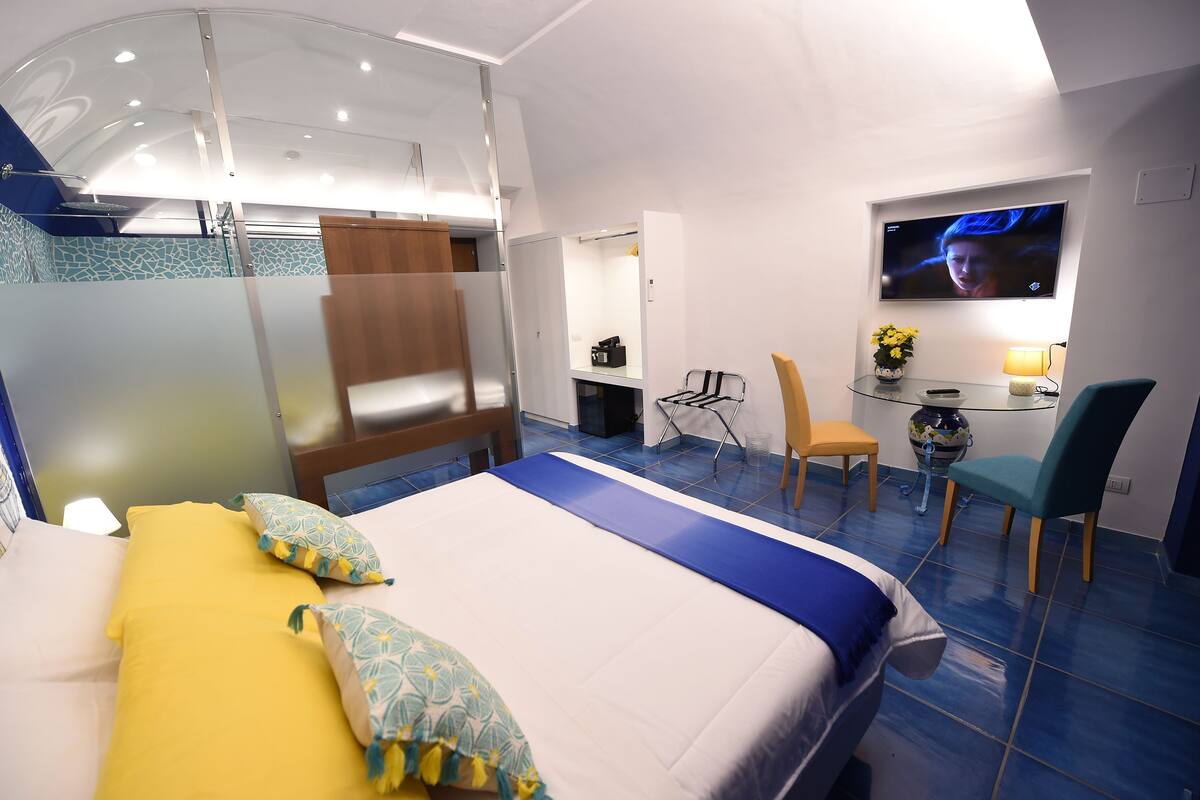 Une chambre d’hôtel avec un lit, un bureau, une télévision et une petite table sur laquelle est posé un vase de fleurs.