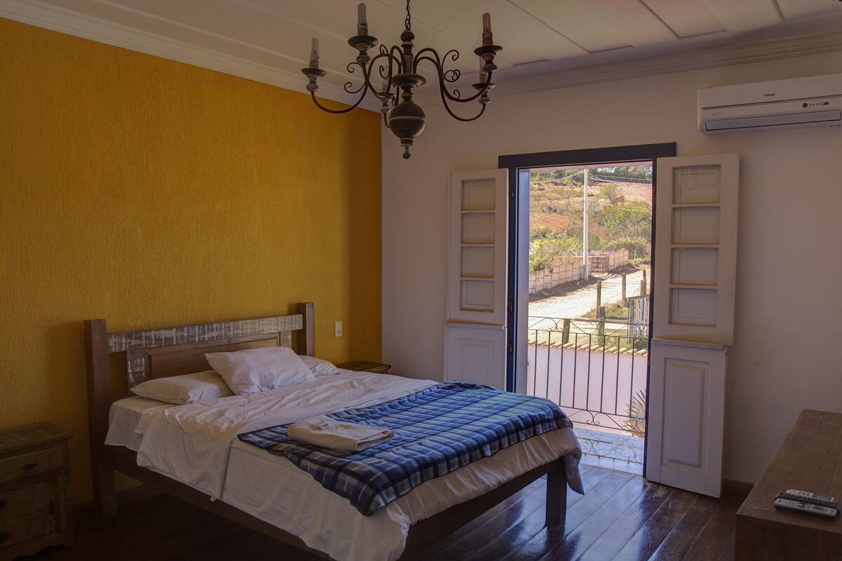 Un dormitorio con una cama de madera, una araña, un equipo de aire acondicionado y vistas al exterior a través de una puerta.