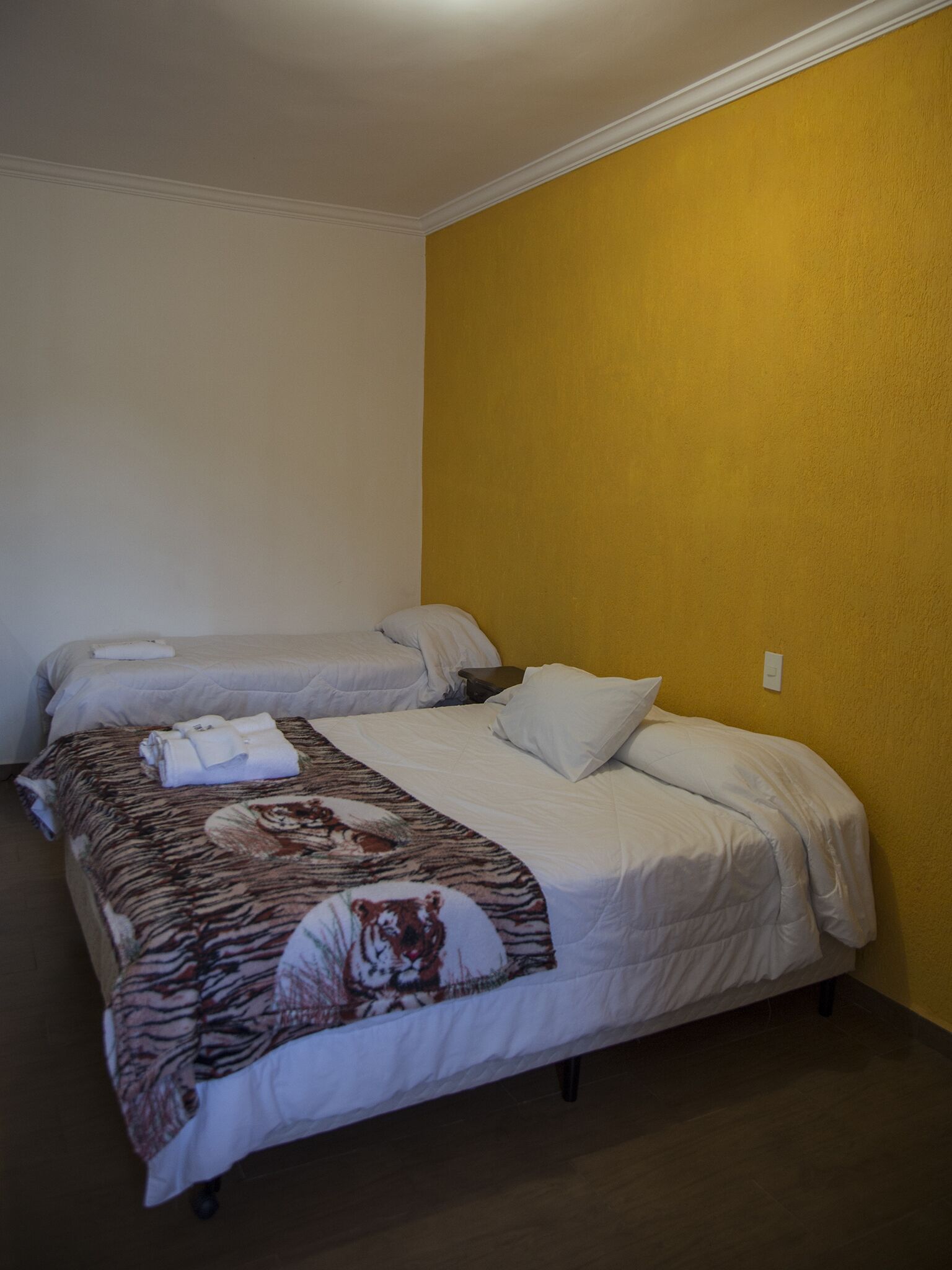 Habitación de hotel con dos camas, una con una colcha estampada de tigre y la otra con ropa de cama sencilla.