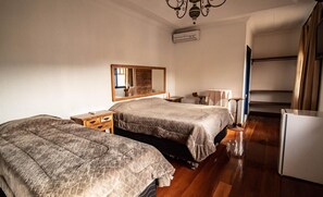 Quarto de hotel com duas camas, um espelho, uma mesinha e uma cadeira.