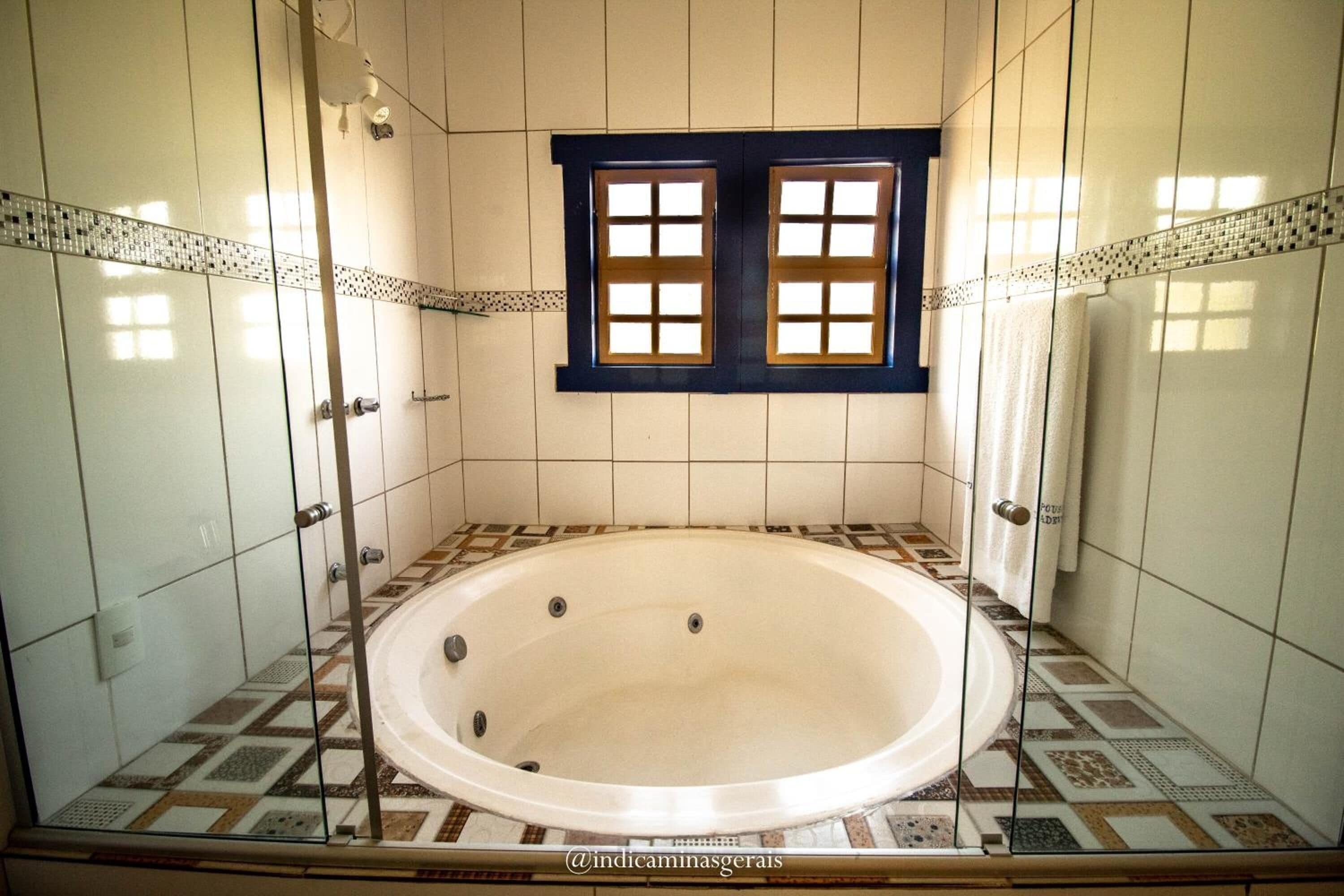 Een badkamer met een groot bad, betegelde wanden en een raam met houten luiken.