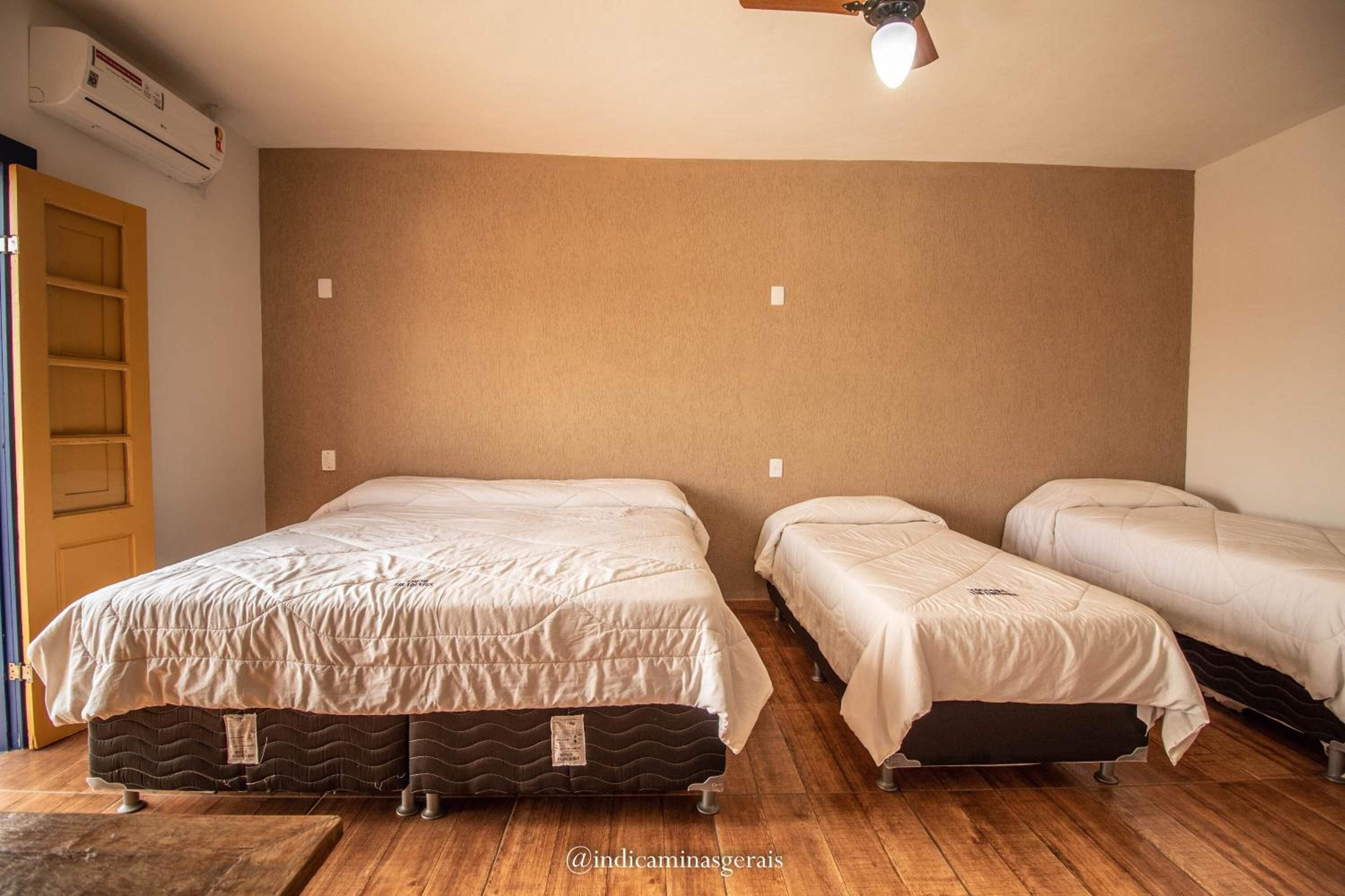 Ein Zimmer mit drei Betten, einem Deckenventilator und einer Klimaanlage.
