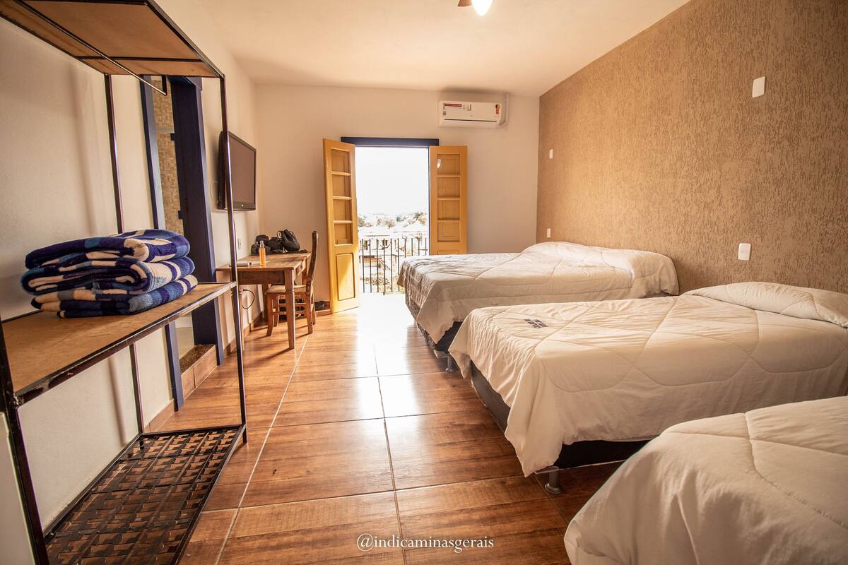 Habitación de hotel con tres camas, un escritorio de madera, una silla y un ventanal grande.