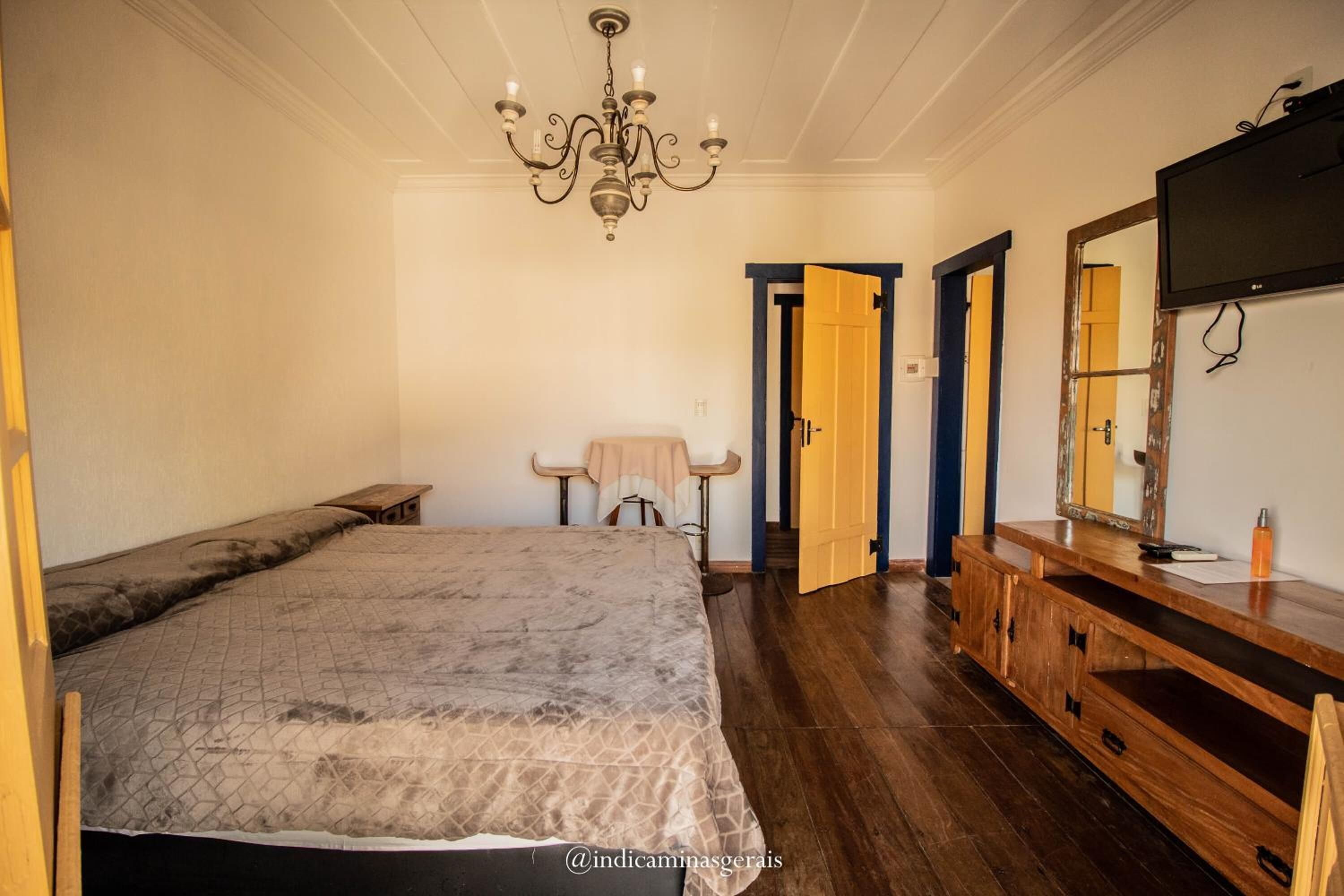 A bedroom with a large bed, a wooden dresser, a mirror, and a chandelier.