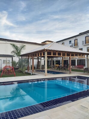 Piscina com deck revestido, área de estar coberta e parquinho.