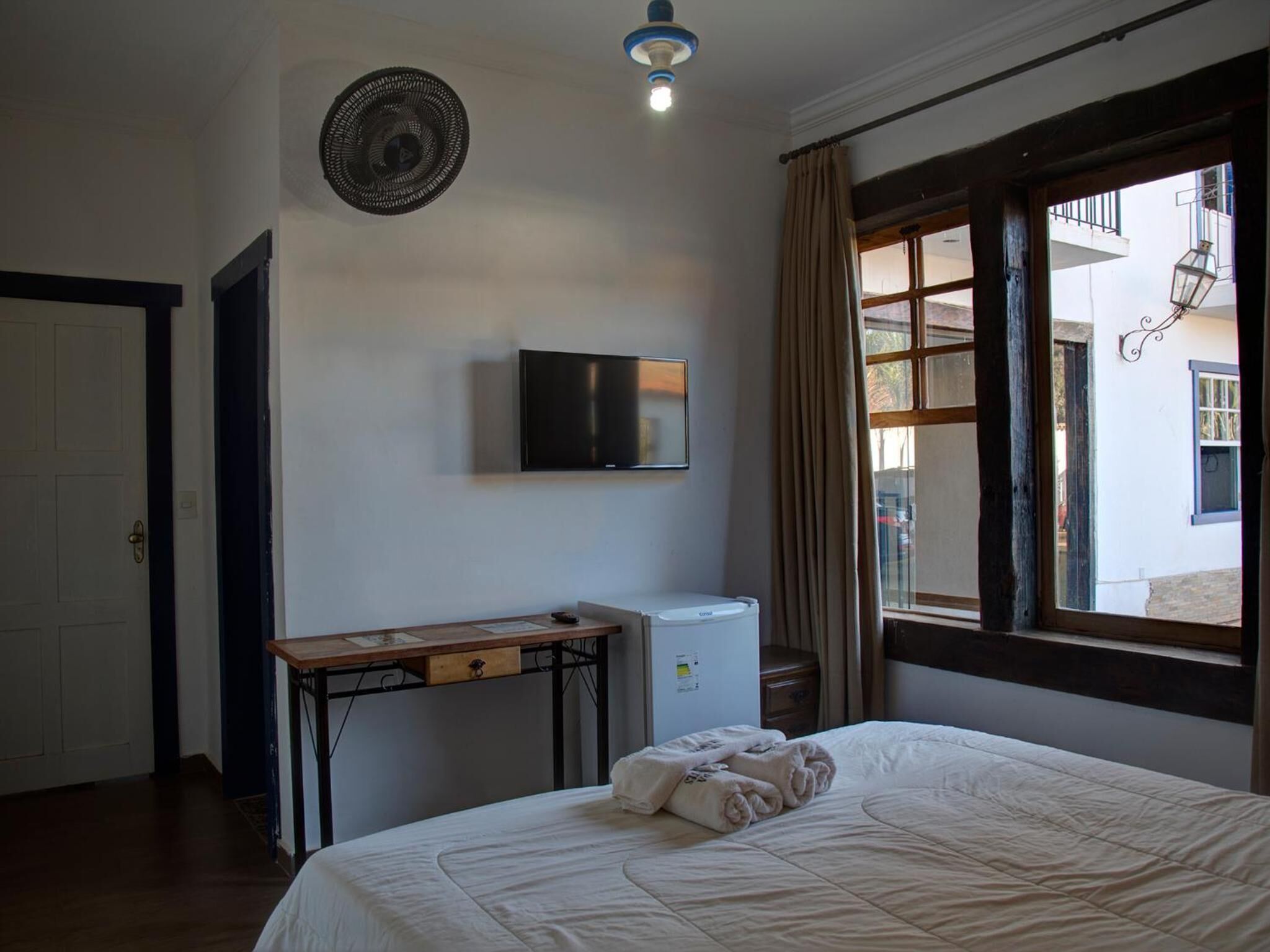 A bedroom with a bed, a desk, a television, and a window with curtains.