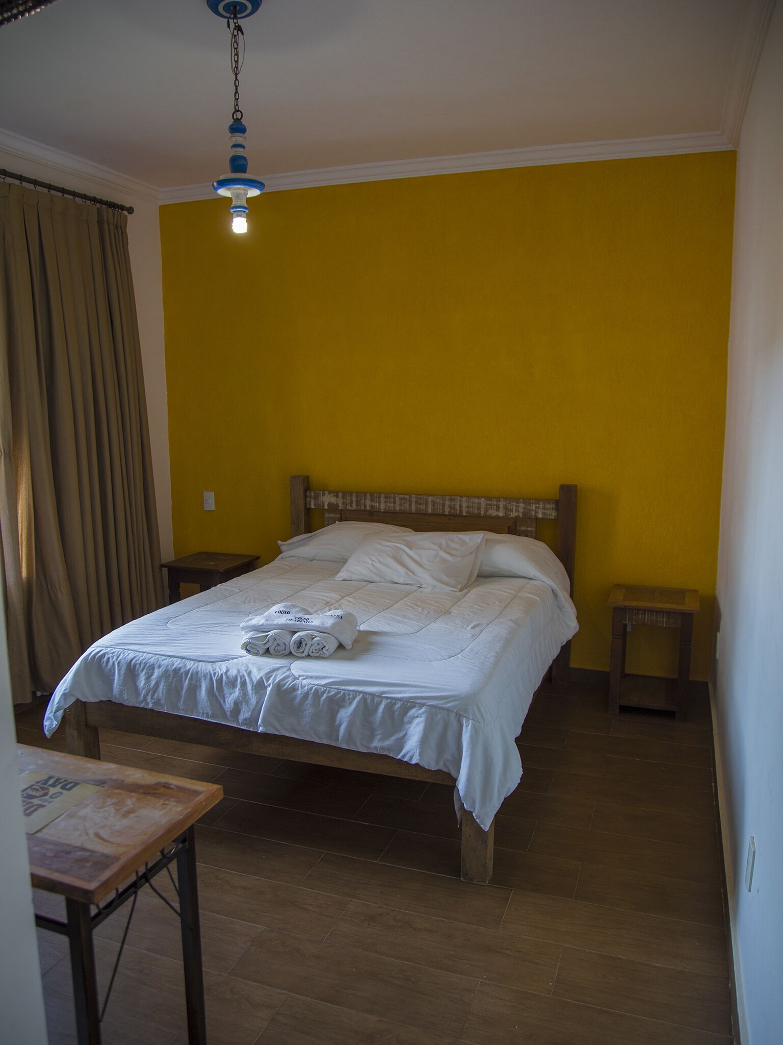 A bedroom with a bed, a wooden headboard, a nightstand, a table, and a hanging light fixture.
