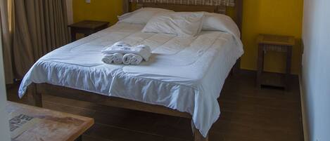 A bedroom with a bed, a wooden headboard, a nightstand, a table, and a hanging light fixture.