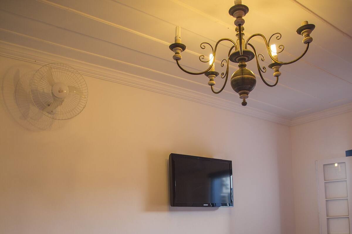 Un dormitorio con cama, televisor montado en la pared, calefactor y un banco de madera.
