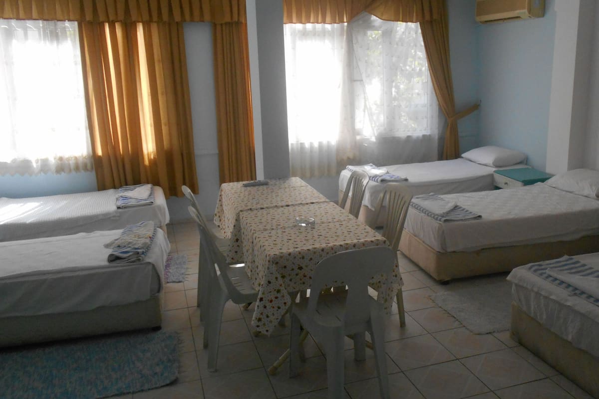 A hotel room with three single beds, a dining table with chairs, and a small table with a chair.
